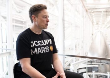 ایلان ماسک با تی‌شرت مشکی "Occupy Mars" در حال نشستن در داخل یکی از سوله‌های صنعتی اسپیس‌اکس.