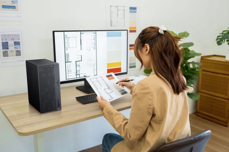 زنی در حال کار با کامپیوتر ایسوس ExpertCenter و بررسی نقشه‌های معماری روی میز کار.