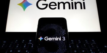 یک گوشی هوشمند با صفحه «Gemini 3» که روی کیبورد لپتاپ قرار گرفته و لوگوی گوگل جمنای در نمایشگر پشت آن دیده میشود.