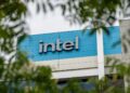 تابلوی لوگوی "intel" روی نمای ساختمان، که از میان شاخ و برگ درختان دیده می‌شود.