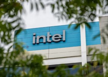 تابلوی لوگوی "intel" روی نمای ساختمان، که از میان شاخ و برگ درختان دیده میشود.