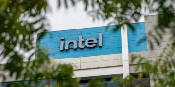 تابلوی لوگوی "intel" روی نمای ساختمان، که از میان شاخ و برگ درختان دیده می‌شود.