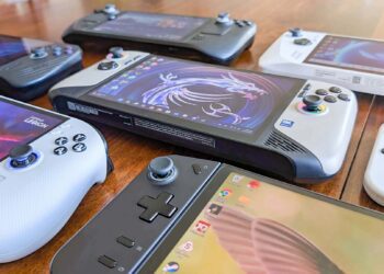 مجموعه‌ای از کنسول‌های بازی دستی مختلف (مانند استیم دک و لنوو لیژن) که روی یک میز چوبی چیده شده‌اند.