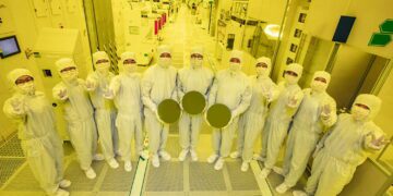 نمای گروهی از کارشناسان در اتاق تمیز کارخانه تولید تراشه سامسونگ، در حال نمایش ویفرهای نیمه‌هادی ۳ نانومتری در محیط صنعتی پیشرفته