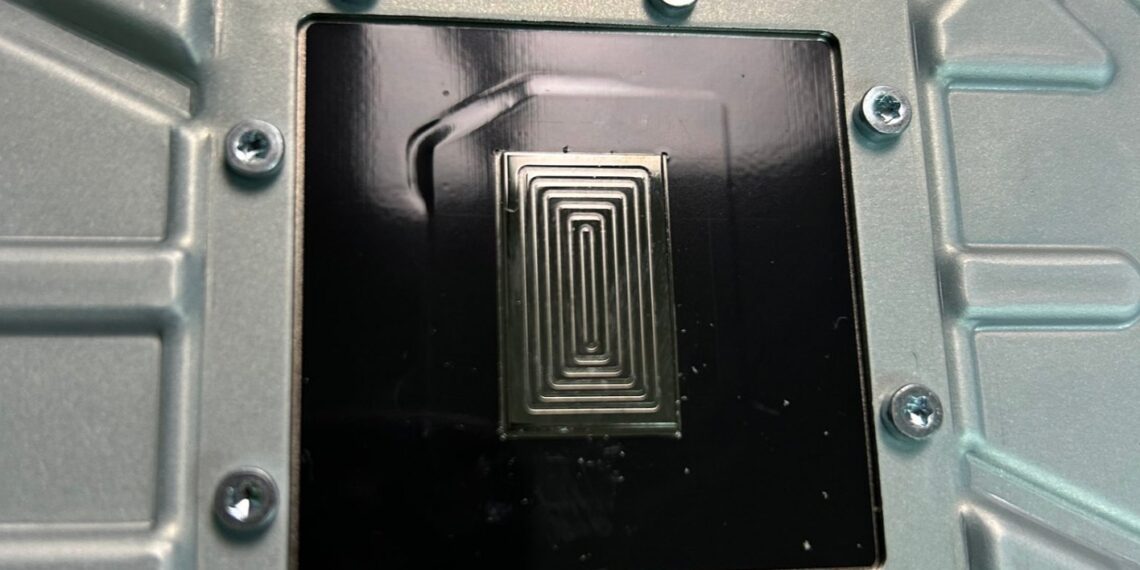 نمای نزدیک از یک سطح فلزی در داخل کنسول PS5 با طرح پیچ در پیچ فلز مایع (TIM) که بر روی سطح مربعی قرار گرفته است.