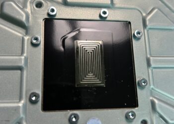 نمای نزدیک از یک سطح فلزی در داخل کنسول PS5 با طرح پیچ در پیچ فلز مایع (TIM) که بر روی سطح مربعی قرار گرفته است.