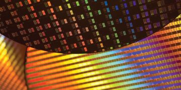 نمای هنری و نزدیک از الگوهای نوری رنگین‌کمانی روی سطح ویفرهای سیلیکونی در خط تولید تراشه.