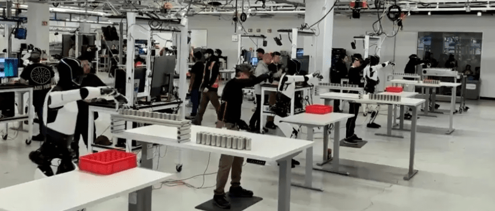 فضای داخلی کارخانه تسلا با چندین ربات اپتیموس که در ایستگاه‌های کاری مشغول تست هستند.