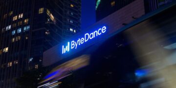 لوگوی نورانی آبی‌رنگ شرکت بایت‌دنس (ByteDance) بر روی نمای ساختمان در شب با پس‌زمینه آسمان‌خراش‌ها.