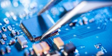 نمای نزدیک از یک تراشه الکترونیکی روی برد آبی رنگ که با استفاده از پنس در جای خود قرار می‌گیرد.