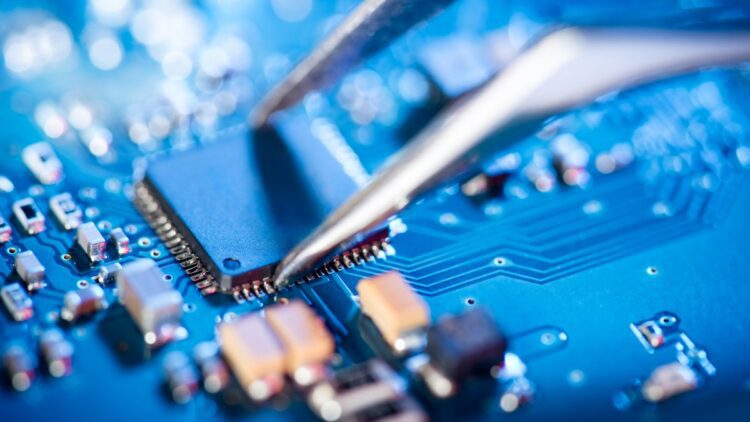نمای نزدیک از یک تراشه الکترونیکی روی برد آبی رنگ که با استفاده از پنس در جای خود قرار میگیرد.