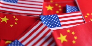 نمای نزدیک از تعداد زیادی پرچمهای کوچک کاغذی ایالات متحده و چین که در کنار هم قرار گرفتهاند.