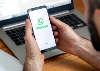 صفحه آغازین اپلیکیشن واتساپ بازشده روی گوشی هوشمند مقابل لپتاپ در حال اجرا، نمایش لوگو و رابط ورود WhatsApp Web