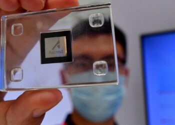 تصویری از نزدیک که یک تراشه هوش مصنوعی Ascend (متعلق به هواوی) را در قاب شیشه‌ای در دست یک فرد نشان می‌دهد.