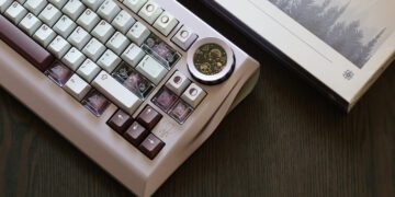 کیبورد مکانیکی Wuque Studio Nama به رنگ بنفش روشن با ناب چرخشی شیشه‌ای که قطعات موتور ساعت را نشان می‌دهد.