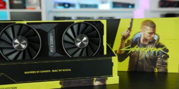 کارت گرافیک اختصاصی NVIDIA RTX 2080 Ti نسخه Cyberpunk 2077 با طراحی زرد و مشکی، قرارگرفته روی پایه نمایش در کنار جعبه بزرگ بازی