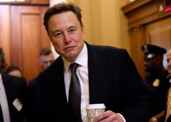 تصویری از ایلان ماسک با پوشش رسمی که یک لیوان قهوه در دست دارد