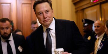 تصویری از ایلان ماسک با پوشش رسمی که یک لیوان قهوه در دست دارد