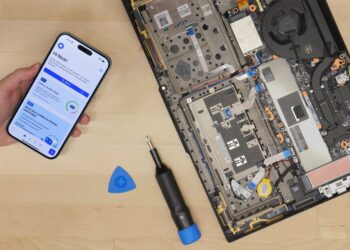 برنامه iFixit روی گوشی آیفون در کنار لپ‌تاپ بازشده و ابزار تعمیر الکترونیکی روی میز کار