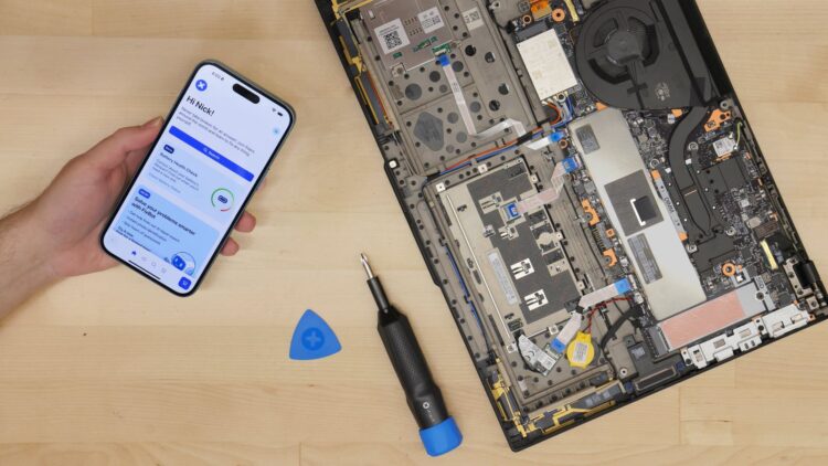 برنامه iFixit روی گوشی آیفون در کنار لپتاپ بازشده و ابزار تعمیر الکترونیکی روی میز کار