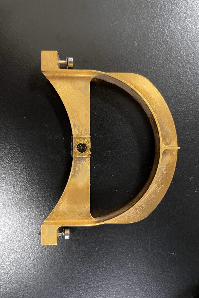 قطعه فلزی نیمدایرهای با یک تراشه میکروسکوپی در مرکز، قرارگرفته روی میز آزمایش.