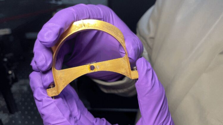 گاه نزدیک به قطعه فلزی U-شکل با تراشه نانویی نصبشده روی پایه مرکزی در دست پژوهشگر با دستکش بنفش