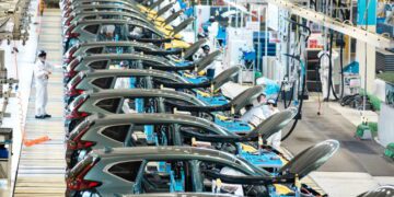 خط تولید خودرو در کارخانه صنعتی با ردیف خودروهای در حال مونتاژ، درهای باز و تجهیزات مکانیزه، نمایش فرآیند تولید انبوه و زنجیره ساخت خودروسازی