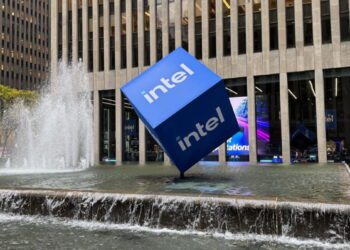 المان تبلیغاتی مکعب آبی Intel نصبشده در مرکز یک آبنمای شهری مقابل ساختمان اداری مدرن؛ تأکید بر برندینگ اینتل، معماری شهری و هویت بصری شرکت فناوری.