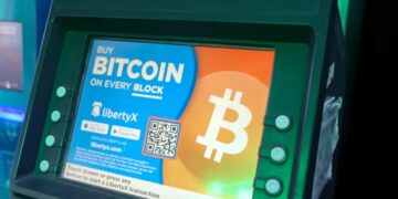 نمای نزدیک از صفحه نمایش یک دستگاه خودپرداز که تبلیغ خرید بیت‌کوین از طریق سرویس LibertyX و اپلیکیشن‌های موبایل را نمایش می‌دهد.