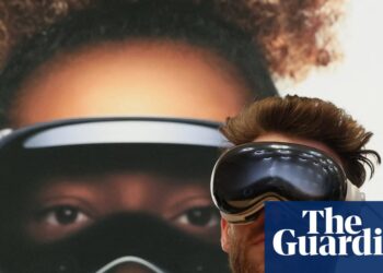 فردی که در حال تست هدست Apple Vision Pro است و پشت سر او تصویر بزرگ تبلیغاتی از این محصول دیده می‌شود.