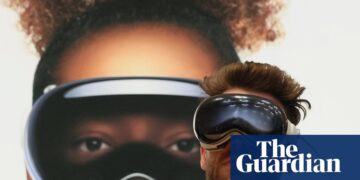 فردی که در حال تست هدست Apple Vision Pro است و پشت سر او تصویر بزرگ تبلیغاتی از این محصول دیده می‌شود.