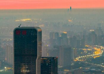 نمای پانوراما از خط افق شهر شانگهای چین در هنگام غروب با ساختمان‌های بلند و بزرگراه‌های پرنور زیر لایه‌ای از مه.