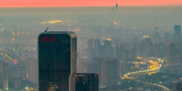 نمای پانوراما از خط افق شهر شانگهای چین در هنگام غروب با ساختمان‌های بلند و بزرگراه‌های پرنور زیر لایه‌ای از مه.