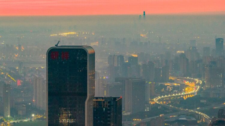 نمای پانوراما از خط افق شهر شانگهای چین در هنگام غروب با ساختمان‌های بلند و بزرگراه‌های پرنور زیر لایه‌ای از مه.
