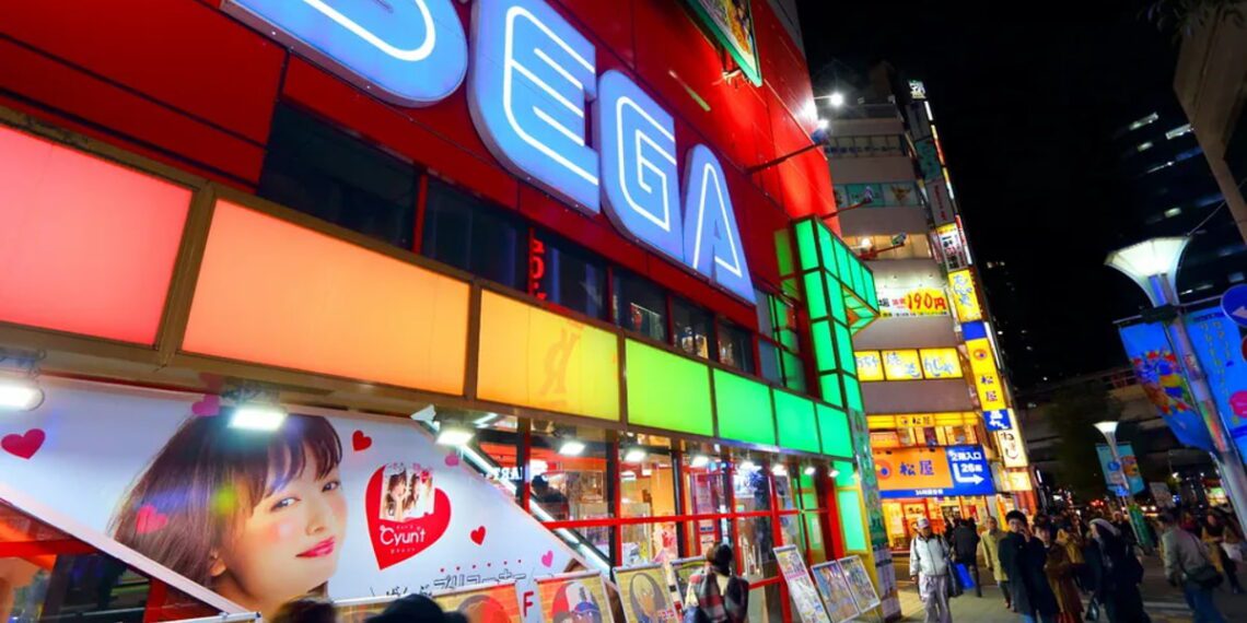 نمای شبانه از یک خیابان تجاری با ساختمان قرمز‌رنگ و تابلوی نورانی بزرگ SEGA، ویترین فروشگاه‌های بازی، پوسترهای تبلیغاتی رنگی و تابلوهای نئونی متعدد در محیط شهری پرنور