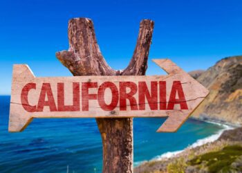 یک تابلوی راهنمای چوبی که فلش آن به سمت راست اشاره دارد و کلمه "CALIFORNIA" با رنگ قرمز روی آن نوشته شده است.