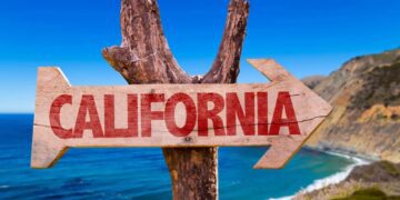 یک تابلوی راهنمای چوبی که فلش آن به سمت راست اشاره دارد و کلمه "CALIFORNIA" با رنگ قرمز روی آن نوشته شده است.