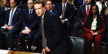 مارک زاکربرگ با کتوشلوار در حال بلند شدن از صندلی در یک جلسه استماع قانونی.