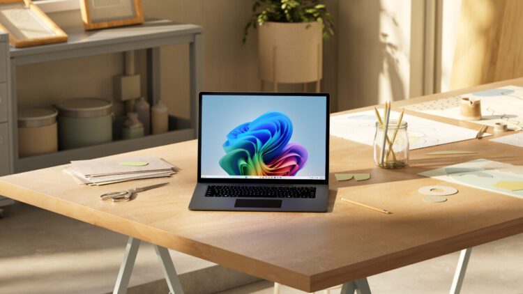 یک لپ‌تاپ باز روی میز کار چوبی که والپیپر آبی ویندوز ۱۱ را نشان می‌دهد و نوری ملایم از پنجره به آن می‌تابد.