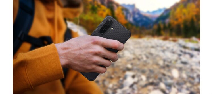 فردی در طبیعت که گوشی هوشمندی با قاب محافظ مشکی و مقاوم در دست دارد.