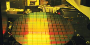 نمایی از داخل یک ماشین صنعتی در کارخانه نیمه‌رسانا که یک ویفر سیلیکونی بزرگ را در فرآیند تولید تراشه نشان می‌دهد.