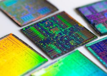 نمای نزدیک از چندین تراشه سیلیکونی نیمه‌هادی با بازتاب رنگی روی سطح.