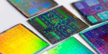 نمای نزدیک از چندین تراشه سیلیکونی نیمه‌هادی با بازتاب رنگی روی سطح.