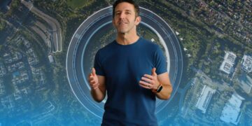 جان ترنوس، مدیر اپل، با تیشرت سرمهای در مقابل نمای هوایی ساختمان Apple Park.