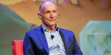 پرترهای از تیم برنرز لی، مخترع وب، با کت سرمهای و پیراهن آبی در یک نشست خبری.