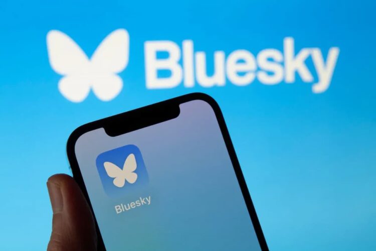 گوشی هوشمندی که آیکون اپلیکیشن Bluesky را نمایش می‌دهد و لوگوی بزرگ Bluesky در پس‌زمینه آن دیده می‌شود.