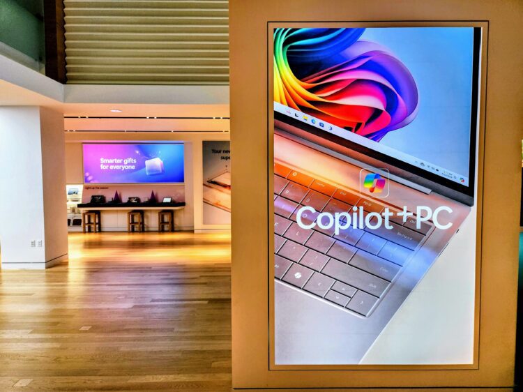 استند تبلیغاتی در یک فروشگاه که لپ‌تاپی با عنوان "Copilot+ PC" را نمایش می‌دهد.