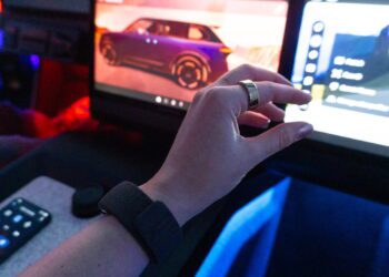 نمای داخلی کابین خودرو با نمایشگرهای دیجیتال داشبورد؛ دست دارای مچ‌بند هوشمند Garmin در حال تعامل با رابط کاربری سیستم اطلاعات‌سرگرمی، نمایش منوها و گزینه‌های کنترلی روی صفحه