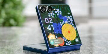 گوشی تاشوی عمودی با طراحی صدفی در حالت نیمهباز روی سطح سنگی، نمایش صفحهنمایش با والپیپر گلدار، ساعت و ویجت هواشناسی، بههمراه ماژول دوربین دوگانه در گوشه بالا