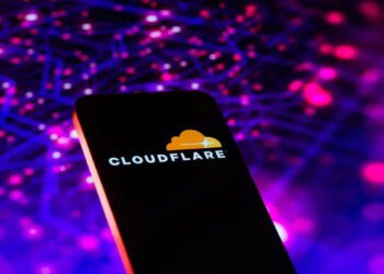 تصویر مفهومی از یک تلفن هوشمند با نمایش لوگوی Cloudflare روی صفحه‌نمایش. پس‌زمینه شامل شبکه‌ای انتزاعی از نقاط و خطوط نورانی به رنگ‌های بنفش و آبی است که مفاهیم زیرساخت شبکه، امنیت ابری و ترافیک داده را القا می‌کند.